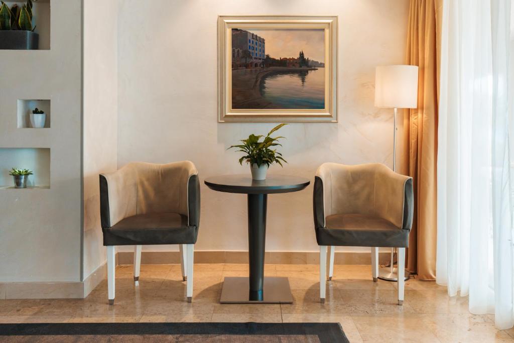 Mūsdienīgs viesistabas stūris ar divām ērtiem krēsliem, elegantu galdu un gleznu uz sienas, radot mājīgu atmosfēru. Aiz galda redzama lampiņa un dabiski elementi, kas papildina interjeru.
