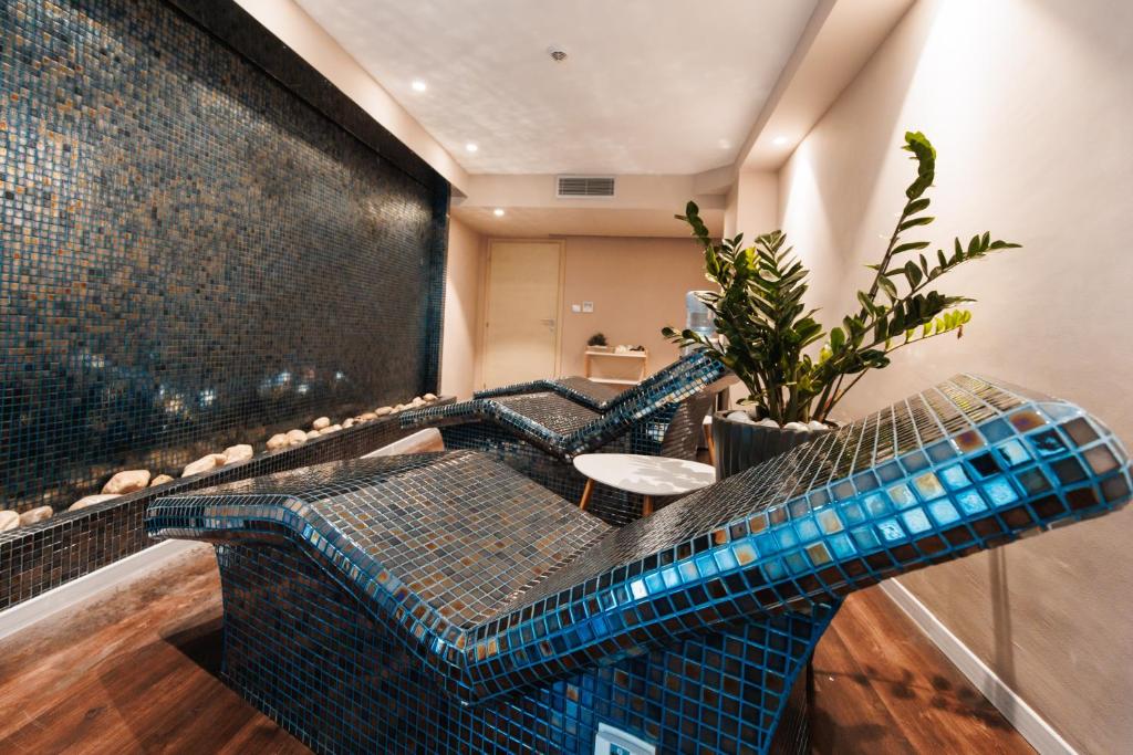 Mūsdienīgs spa telpa ar mozaīkas dizainu, kurā redzami atpūtas krēsli un zaļš augs, radot relaksējošu atmosfēru.