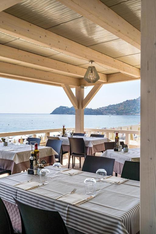 Jūras tuvumā esošs restorāns ar elegantiem galdiem un skatu uz ūdeni, kas radīja mierīgu un relaksējošu atmosfēru.