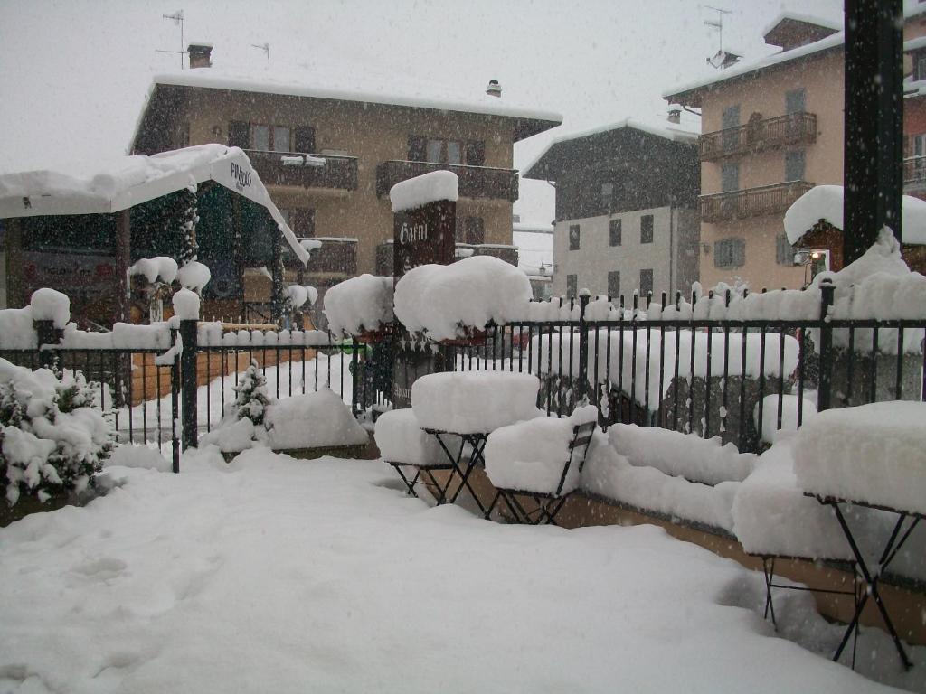 Sniega segtu dārzu ar soliņiem un galdiem, apkārtējās ēkas un sniegainais skats. Sniegs klāj visu apkārtni, radot ziemīgu atmosfēru.