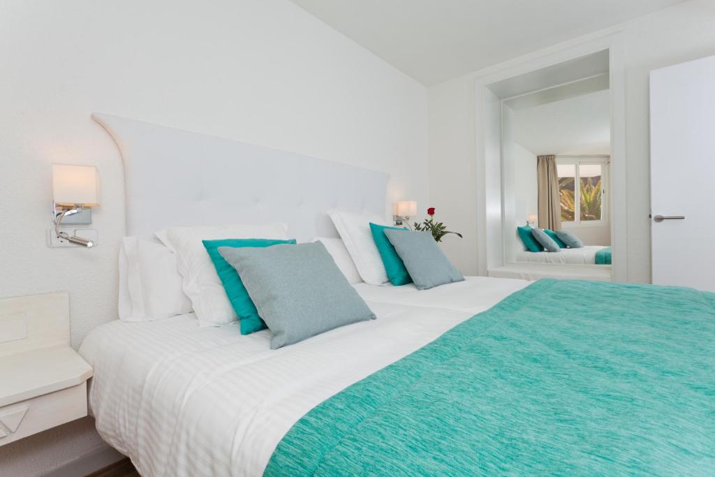 Mūsdienīga guļamistaba ar divguļamo gultu, dekorēta ar zilu un pelēku spilvenu, un spoguli, kas atspoguļo dabas gaismu. Elegants un komfortabls interjers rada viesmīlīgu atmosfēru.