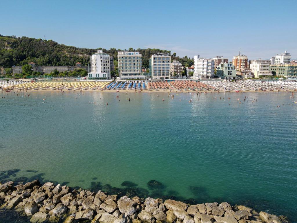 Pludmale ar saules gultām un cilvēkiem, kas bauda ūdeni, fons ar viesnīcām un kalnu. Skats uz mierīgu jūru un akmeņainu krastu.