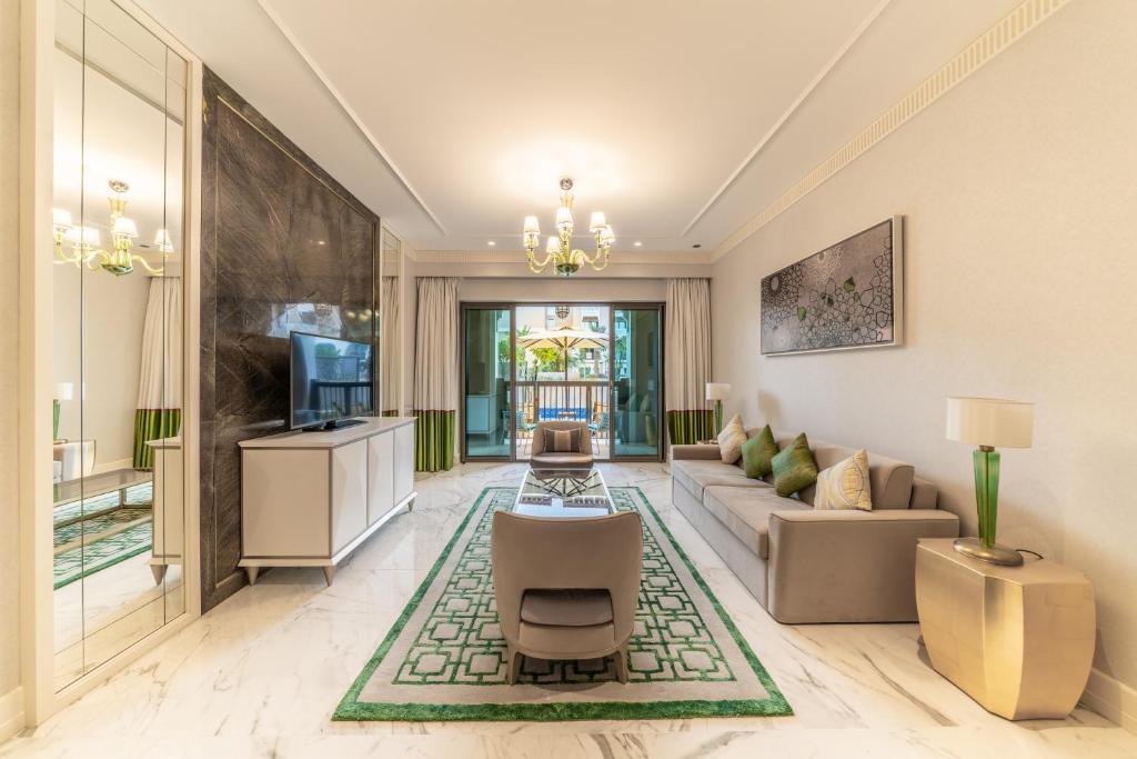 Mūsdienīgs viesistabas interjers ar elegantu dizainu, kurā ir dīvāns, TV un piekļuve balkonam. Telpā ir gaismas krēslus un dekoratīvas detaļas, radot patīkamu atmosfēru.