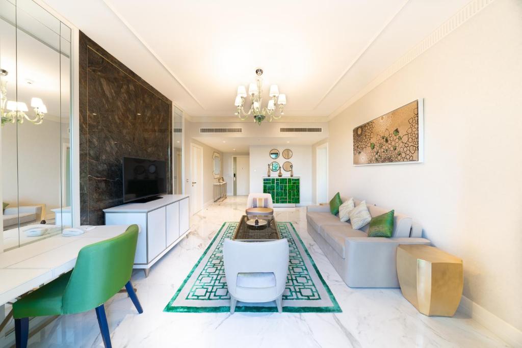 Mūsdienīgs viesistaba ar elegantiem zaļiem akcentiem, baltām sienām un marmora grīdu, kas izceļ šika mēbeles un mākslas darbus. Interjers ir gaišs un plašs, radot komfortablu atmosfēru.
