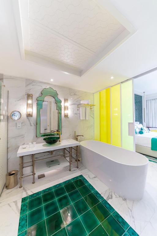 Mūsdienīgs vannas istabas interjers ar greznu zaļo flīžu grīdu, elegantu brīvi stāvošu vannu un stilīgu spoguli. Telpu papildina gaiši toņi un mūsdienīgi apgaismojuma risinājumi.