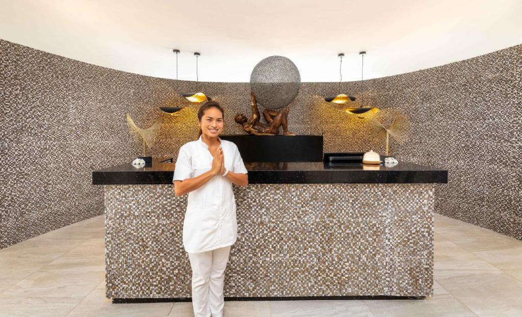 Spa centra recepcija ar laipnu darbinieku, kas sveicina apmeklētājus. Sienas dekorētas ar mozaīkas akmeņiem, radot mierīgu atmosfēru.