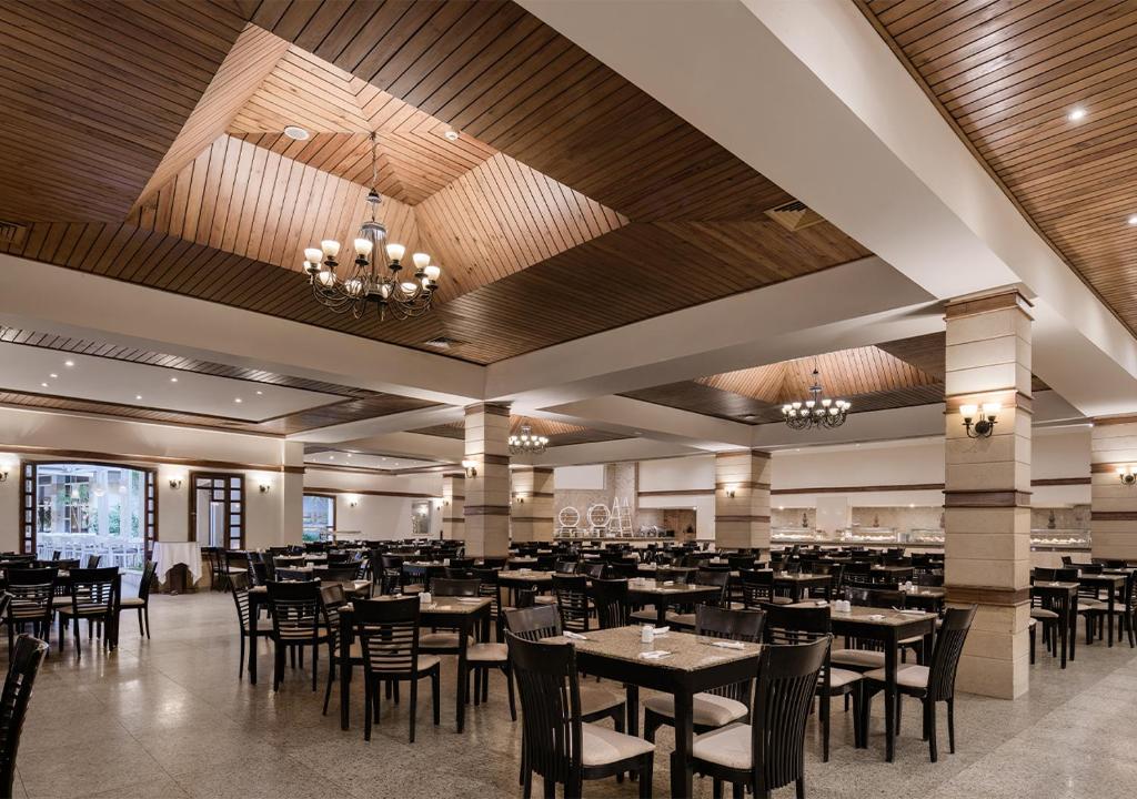 Plaša un moderna restorāna iekārtojums ar koka griestiem, elegantiem apgaismojumiem un daudzām galdiem. Telpa ir gaiša un viesmīlīga, radot patīkamu atmosfēru.