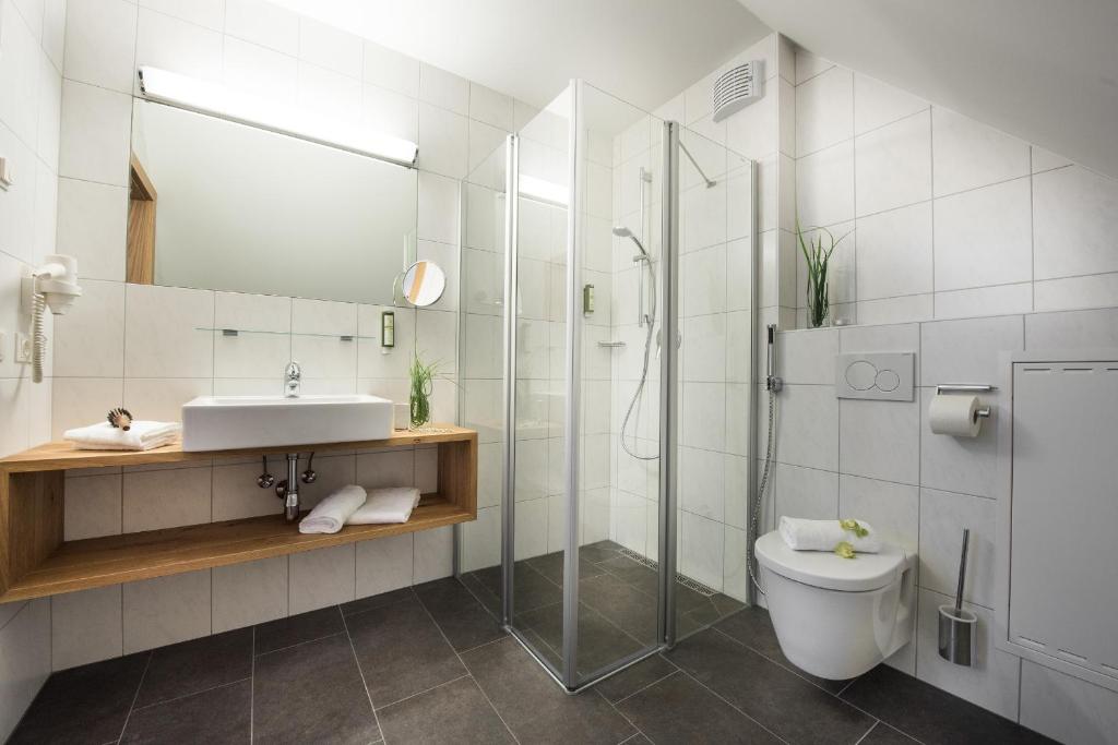 Mūsdienīgs vannas istabas dizains ar stikla dušas kabīni, pelēku flīžu grīdu un koka izlietni. Interjers ir gaišs un elegants, radot patīkamu atmosfēru.