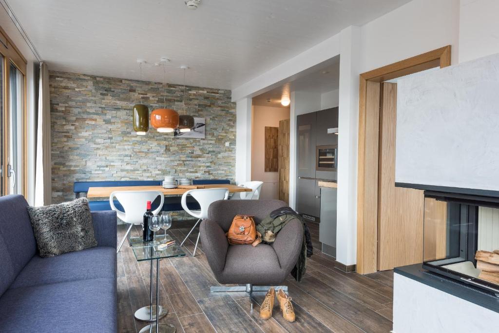 Mūsdienīgs dzīvojamās telpas interjers ar akmens sienu, ērtu dīvānu un stilīgu ēdamgaldus. Gaismas ķermeņi piešķir siltumu un eleganci telpai.