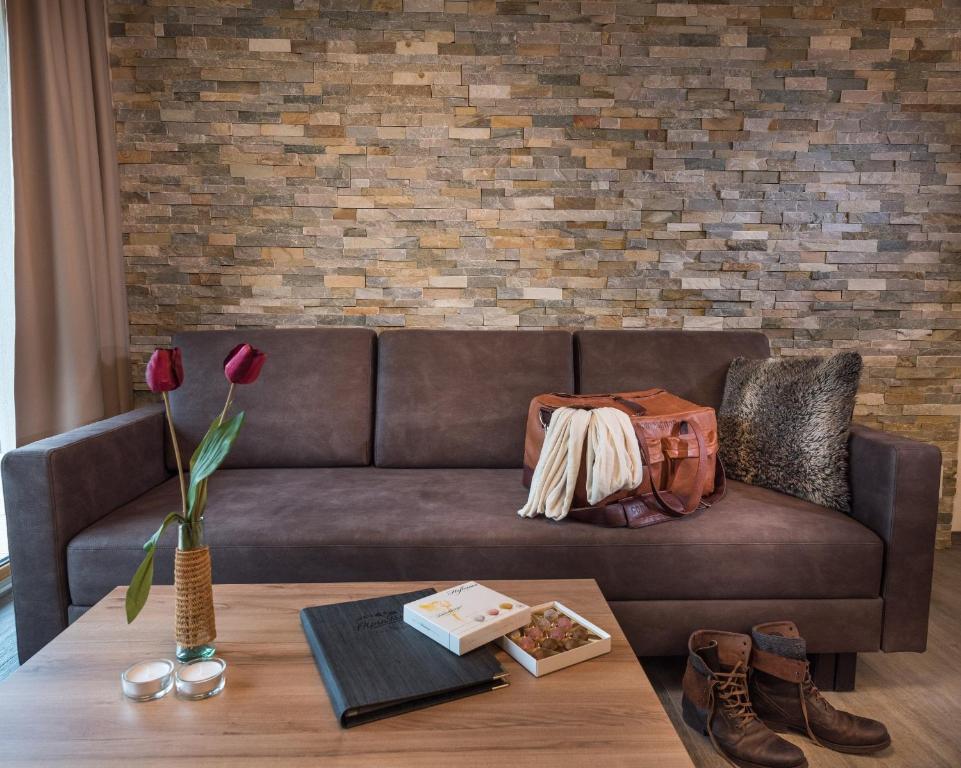 Mūsdienīga dzīvojamā istaba ar brūnu dīvānu, akmens sienu un dekoratīviem elementiem, piemēram, ziediem un bagāžu. Interjers izskatās silts un viesmīlīgs.