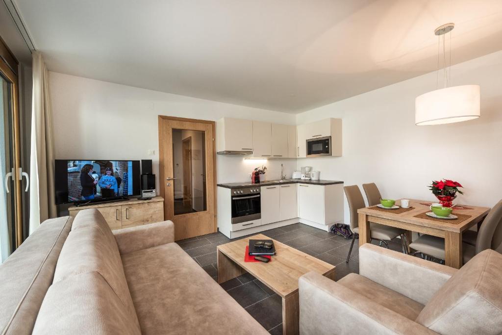 Mūsdienīgs dzīvojamās telpas interjers ar atvērtu virtuvi, ēdamgaldu un ērtu dīvānu. Telpā ir televizors un gaismas avots, radot mājīgu atmosfēru.