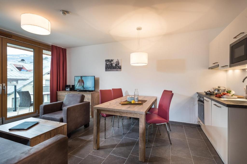 Mūsdienīgs viesistabas interjers ar koka mēbelēm, ēdamgaldu un televizoru, kas piedāvā komfortu un mājīgumu. Logi nodrošina dabīgu apgaismojumu un skatu uz ārpusi.