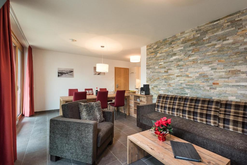 Mūsdienīgs viesistabas interjers ar akmens sienu, ērtām mēbelēm un ēdamzona. Telpā ir lieli logi, kas nodrošina dabisko apgaismojumu, un dekoratīvas augu kompozīcijas.