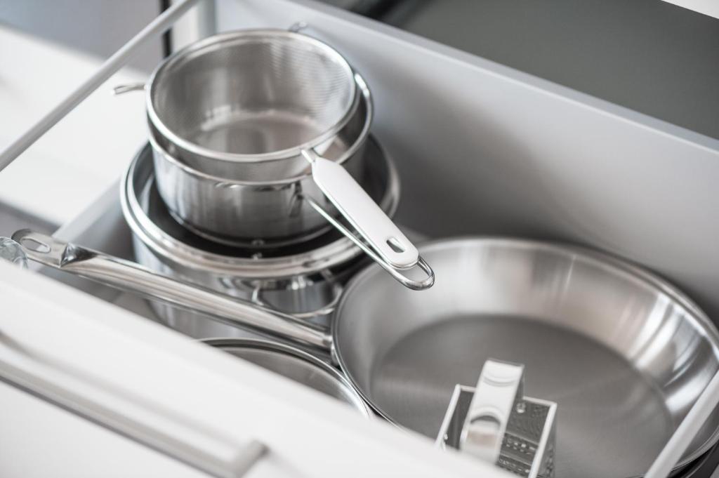 Metāla virtuves trauku un piederumu komplekts, kas organizēts atvilktnē. Tajā ietilpst katli, sietiņi un rīve.