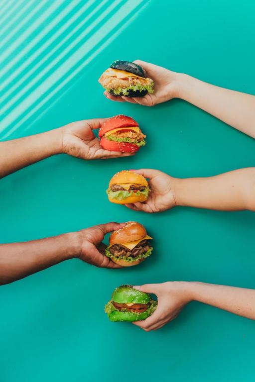 Krāsaini burgeri rokās uz spilgti zaļas virsmas.