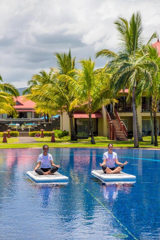 Divi cilvēki meditē uz pludiņiem pie Tamassa Bel Ombre baseina.