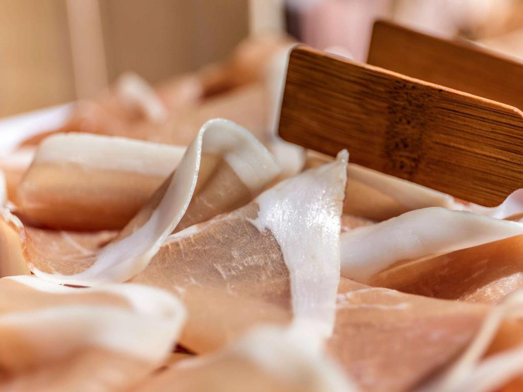 Plāni sagriezti gaļas šķēlītes uz pasniegšanas galda, ar koka pārtikas rīku.