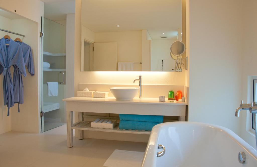 Mūsdienīgs un gaišs vannas istabas interjers ar lielu spoguli, baltu izlietni un mīkstiem halātiem. Vannas istabā ir arī krāsainas higiēnas preces un plaukti ar dvieļiem, radot relaksējošu atmosfēru.