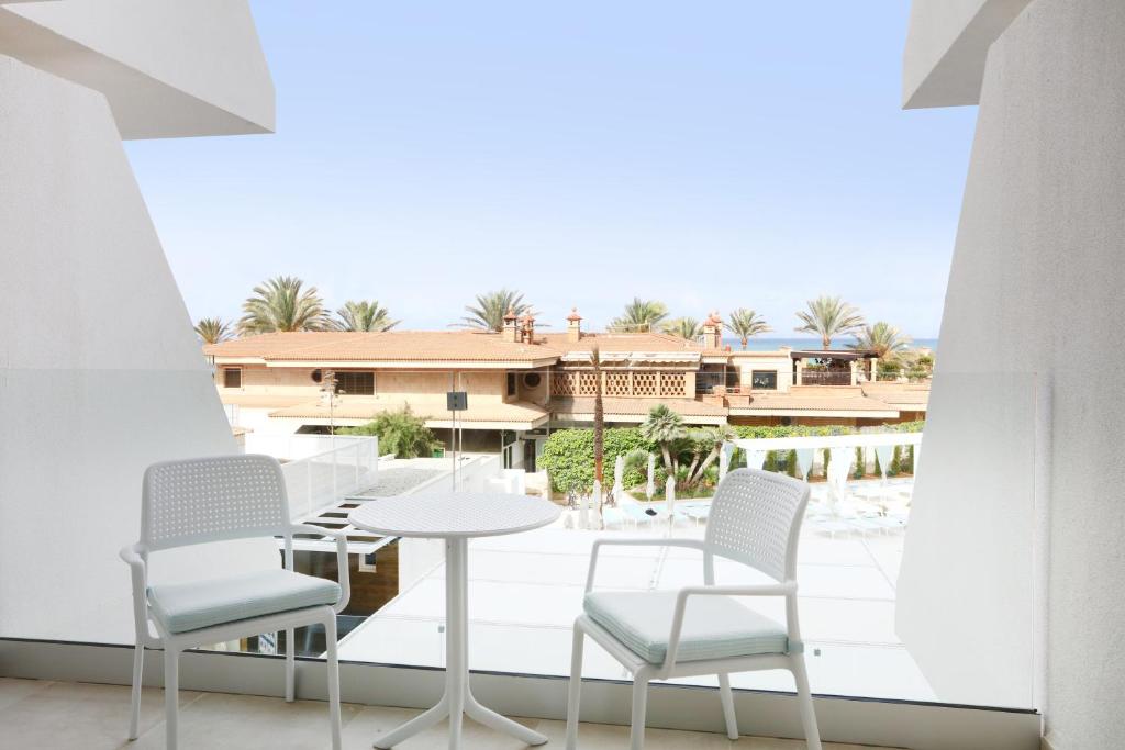 Balkons ar divām baltām krēsliem un mazu galdiņu, no kura paveras skats uz viesnīcu un palmu kokiem. Ideāla vieta relaksācijai un baudīšanai.