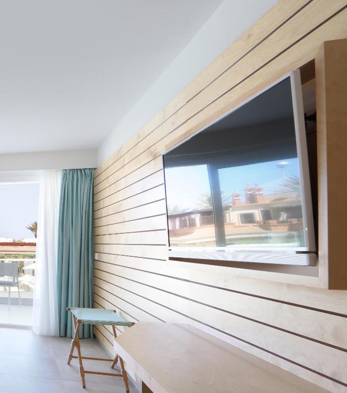 Mūsdienīga viesnīcas istaba ar koka sienām, televizoru un gaišiem aizkariem. Daba redzama caur logu, radot relaksējošu atmosfēru.