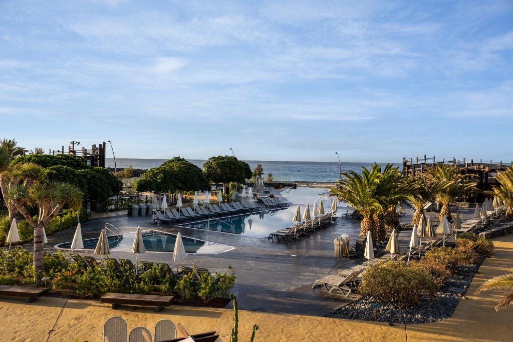 Luksusīgs kūrorta baseins ar palmām un smilšu pludmali, skats uz jūru un skaidru debesu fonu. Ideāla vieta atpūtai un relaksācijai.