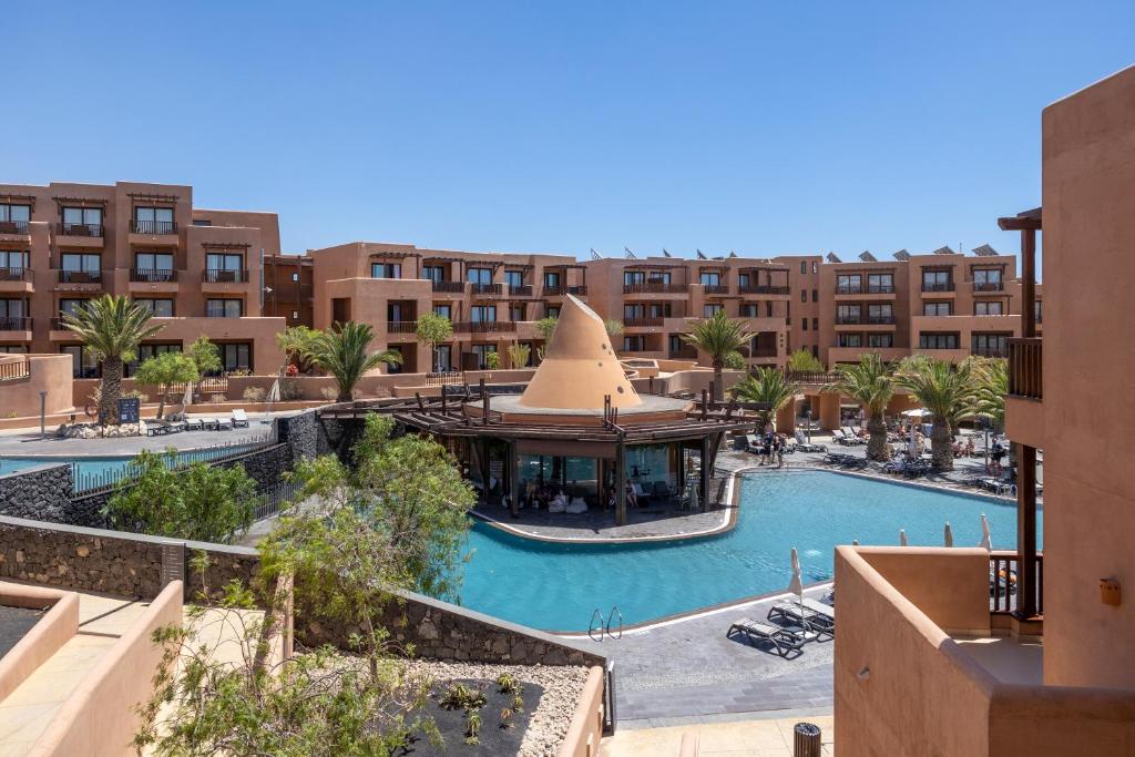 Luksusa viesnīca ar baseinu un palmām, kas atrodas saulainā vietā. Viesnīcas arhitektūra un apkārtējā vide rada relaksējošu atmosfēru.