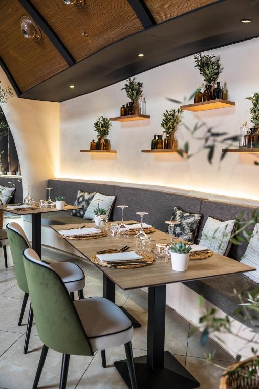 Mūsdienīgs restorāna interjers ar elegantiem galdiem, dekorētiem ar augu kompozīcijām un glāzēm. Siltā apgaismojumā un patīkamā atmosfērā ir redzami ērti krēsli un stilīgi aksesuāri.