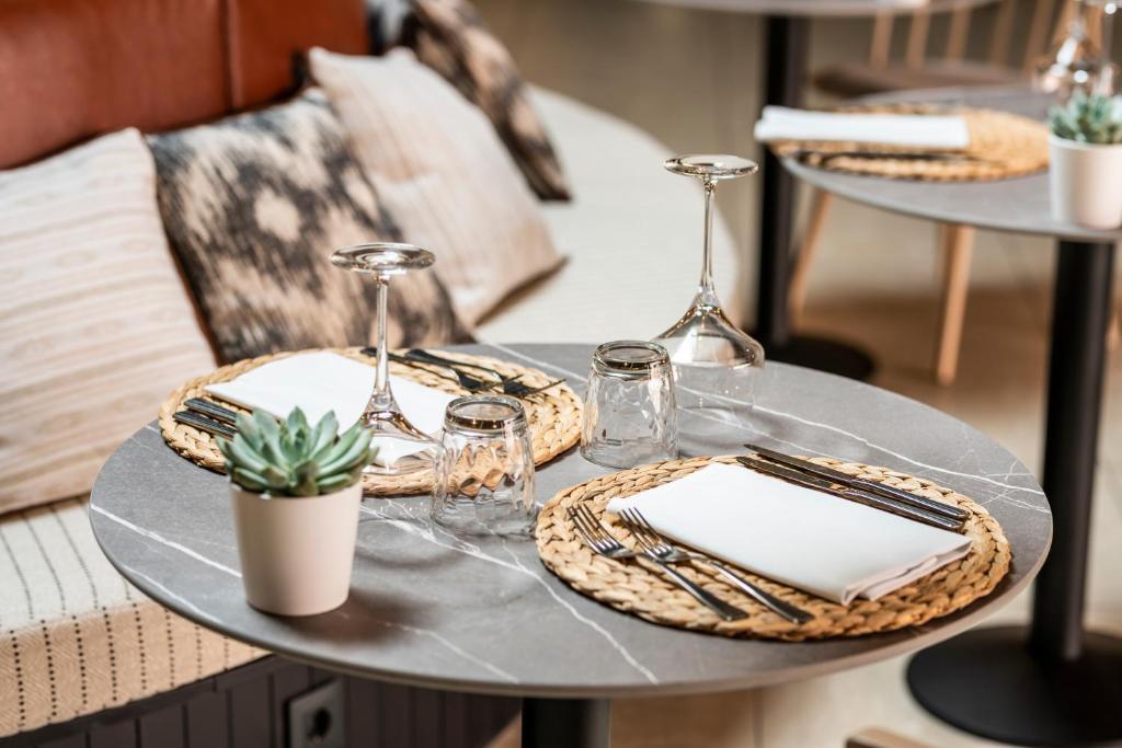 Elegants galda iestatījums restorānā ar vīna glāzēm, stikla traukiem un salvetēm uz pīta paliktnīša. Uz galda ir arī neliela sukulentu podiņš, radot mājīgu atmosfēru.