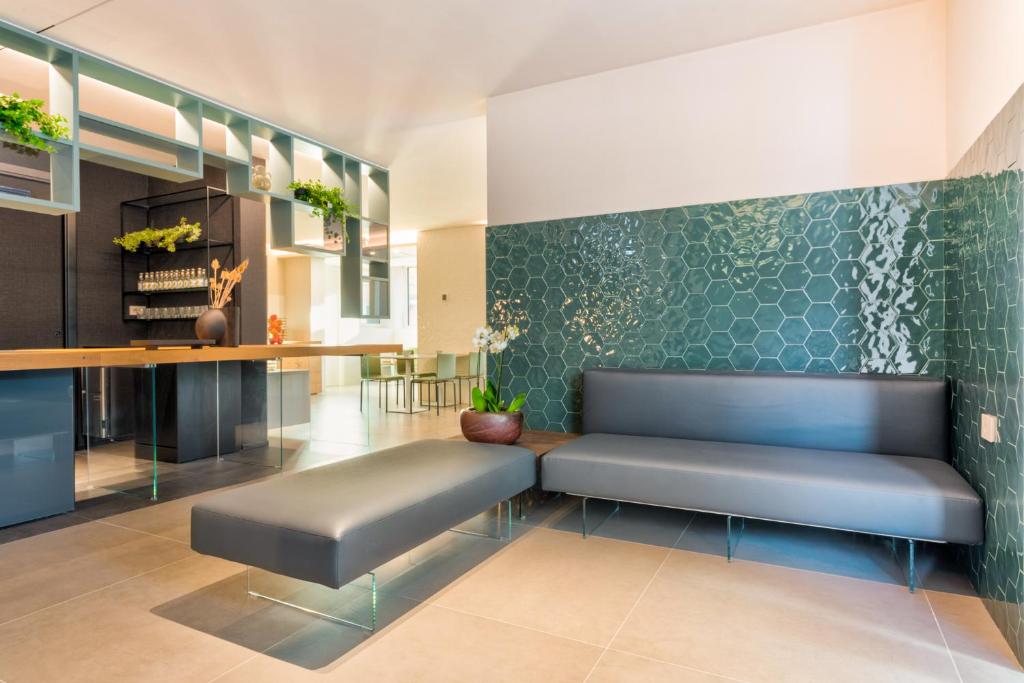 Mūsdienīgs viesnīcas interjers ar pelēku dīvānu un zaļu flīžu sienu.