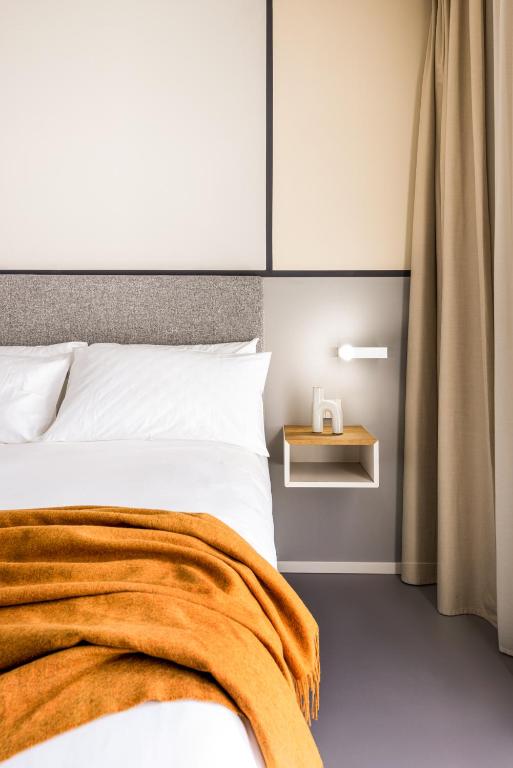 Moderns viesnīcas numurs ar baltu gultu un oranžu segu.