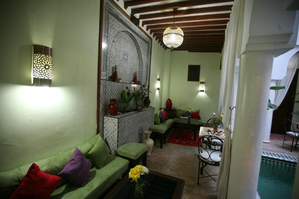 Mūsdienīgs interjers ar zaļām dīvānu zonām un dekoratīvām lampām, kurā redzama marokāņu stila apdare un ziedu kompozīcijas. Telpa ir silta un aicinoša, ideāli piemērota relaksācijai.
