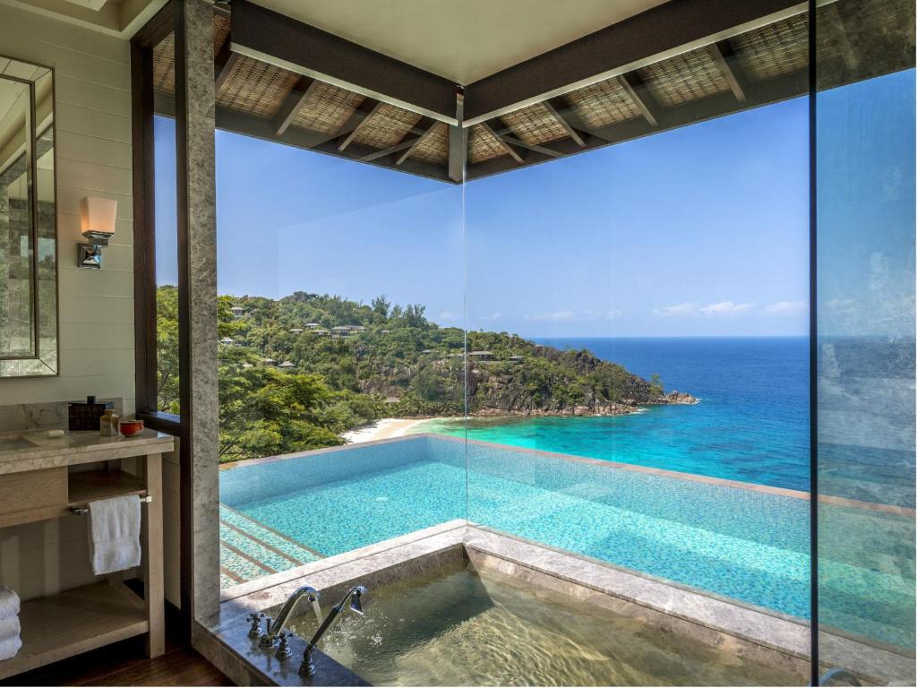 Four Seasons Resort Seychelles numura vannas istaba ar panorāmas logiem un skatu uz okeānu.