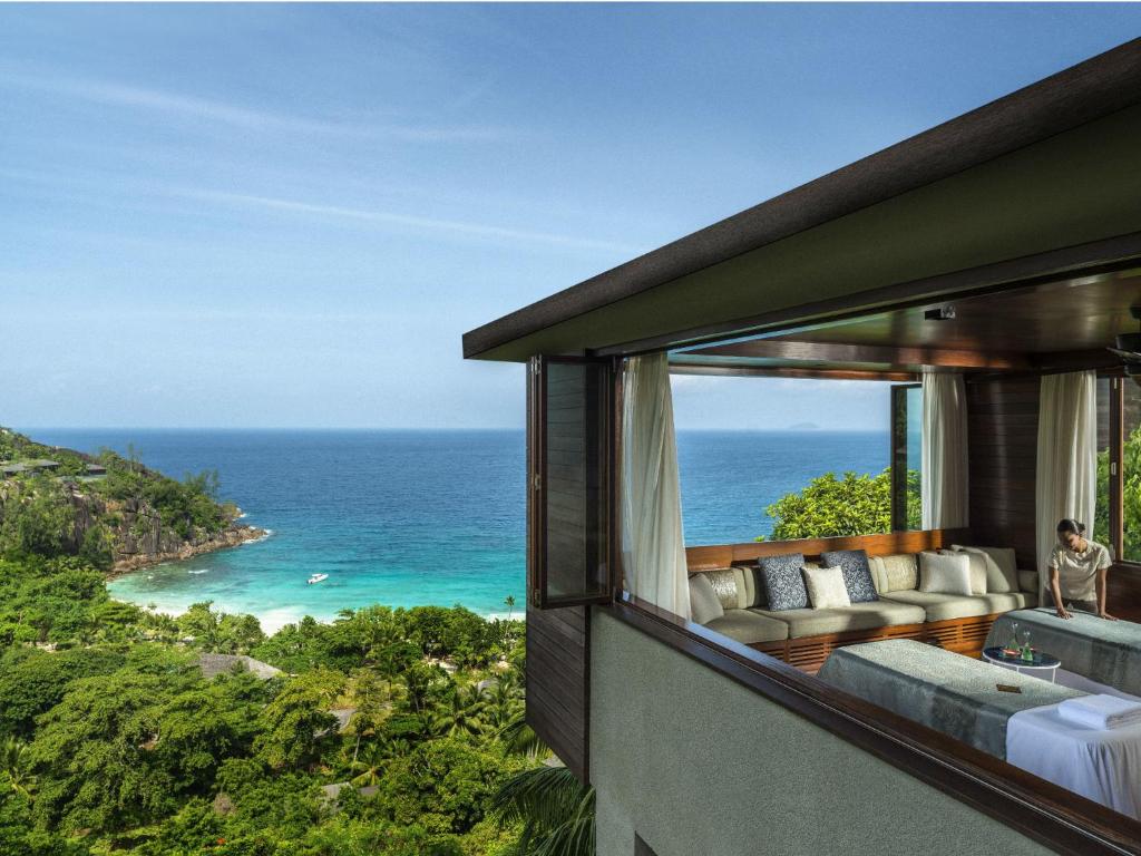Four Seasons Resort Seychelles spa paviljons ar atvērtiem logiem un skatu uz tirkīzzilo okeāna līci un tropu mežu.