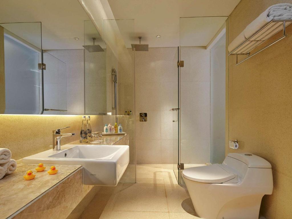 Mūsdienīgs vannas istabas interjers ar stikla dušas kabīni, elegantu izlietni un modernu sanitāro iekārtu. Izskatās tīrs un stilīgs, ar dekoratīviem elementiem.