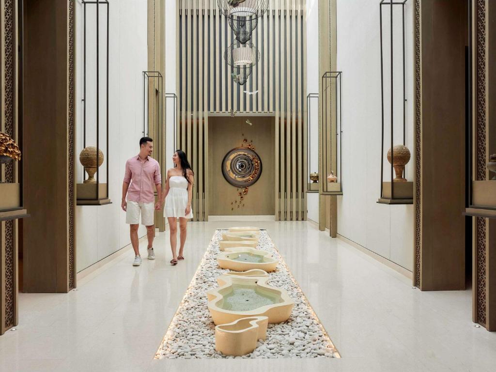 Romantiska pāris pastaiga cauri elegantiem interjera elementiem, kas rotā plašu koridoru ar dekoratīviem traukiem un relaksējošu ūdens plūsmu. Mūsdienīgs dizains un harmoniska atmosfēra rada siltu un viesmīlīgu noskaņu.