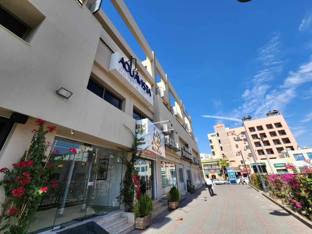 Moderns viesnīcas ēkas skats ar dārza elementiem un skaidru zilu debesi. Ap ēku ir ziedi un augu dekorācijas.