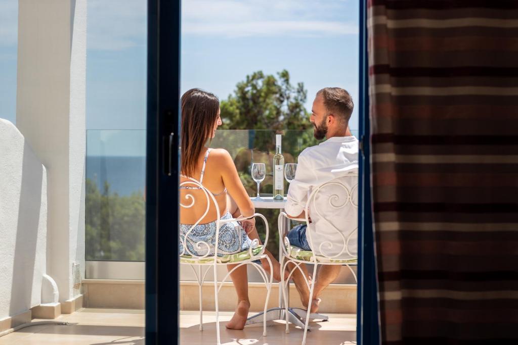 Pāris sēž uz terases, baudot vīnu un skatu uz jūru. Apskates vieta ir gaiša un saulaina, radot romantisku atmosfēru.