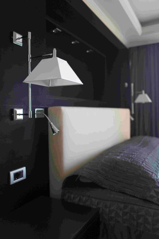 Mūsdienīgs guļamistabas interjers ar melnu sienu, gultas galvgaļu un stilīgām lampām, radot elegantu un relaksējošu atmosfēru.