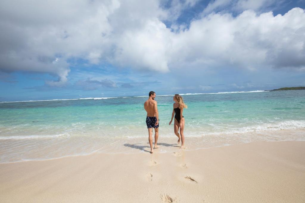 Pāris pastaigā gar pludmali, baudot saulainu dienu un skaistu jūru. Zilais ūdens un smilšu krasts veido idillisku ainavu.