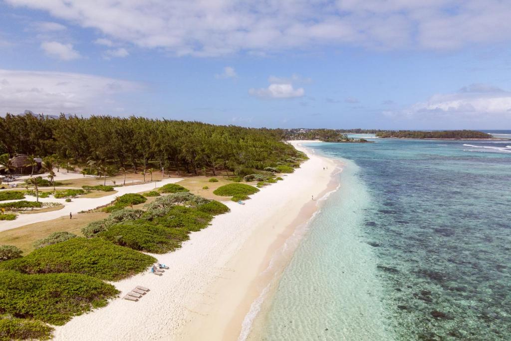 Smilšaina pludmale ar zaļiem krūmiem un kokosriekstu palmām, kas sniedzas gar skaidru, zilu ūdeni. Ideāla vieta atpūtai un dabas baudīšanai.