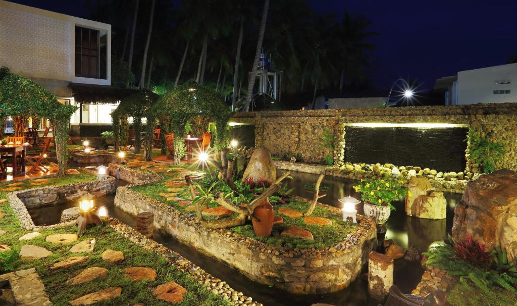 Skaists dārza ainava naktī ar gaismiņām, akmeņiem un ūdens strūklaku, radot mierīgu atmosfēru. Dārza elementi un koki veido burvīgu pievilcību.