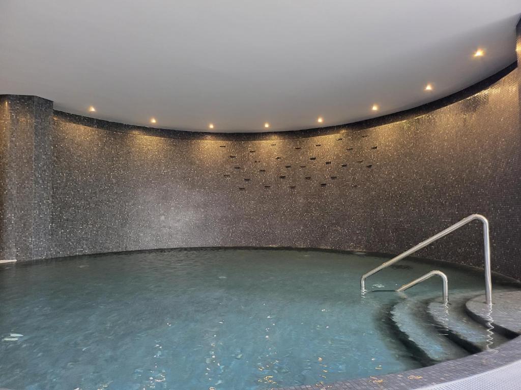 Mūsdienīga un relaksējoša spa telpa ar taisnstūrveida baseinu, kurā ir zema apgaismojuma atmosfēra un akmens mozaīka uz sienām.