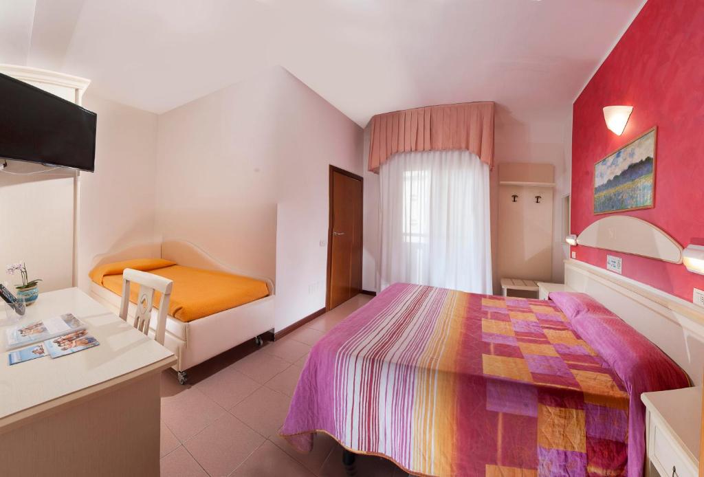 Mūsdienīga viesnīcas istaba ar divguļamo gultu un vienguļamo gultu, kas aprīkota ar televizoru un dabiskiem gaismas avotiem. Sienas rotā krāsains dekors, radot mājīgu atmosfēru.