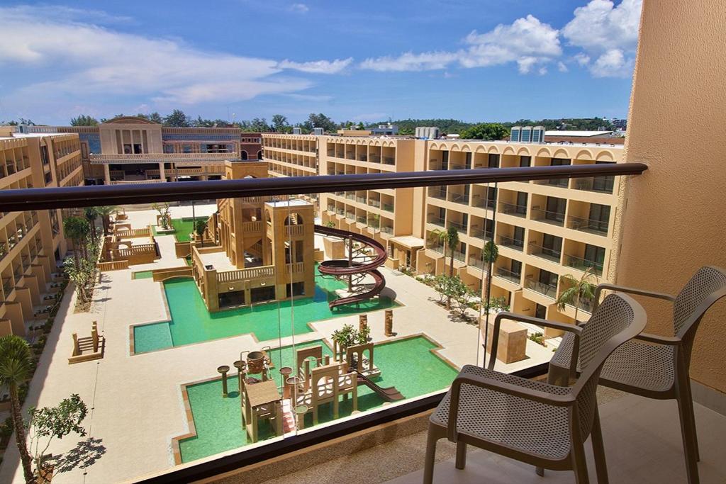 Balkons ar skatu uz viesnīcas iekšpagalmu, kur atrodas baseins un ūdens slidkalniņš. Apkārt ir zaļumi un atpūtas zonas.