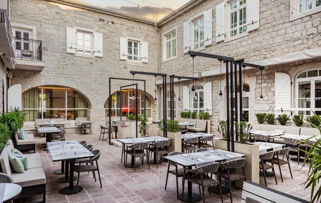 Moderns restorāns ar āra terasi, kurā redzamas elegantas galdi un krēsli, kā arī akmens sienas un zaļumi. Ideāla vieta relaksējošai maltītei.