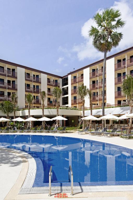 Lielisks viesnīcas baseins ar palmām un saulessargiem, kas atrodas skaistā, zaļā vidē. Apburoša arhitektūra un skaidrs debesis rada relaksējošu atmosfēru.