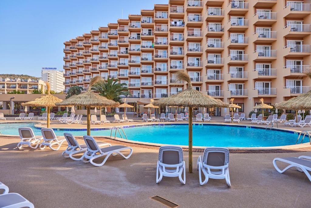 Baseins ar sauļošanās krēsliem un palmu koku foniem, viesnīcas ēka ar balkoniem. Ideāla vieta atpūtai un relaksācijai.