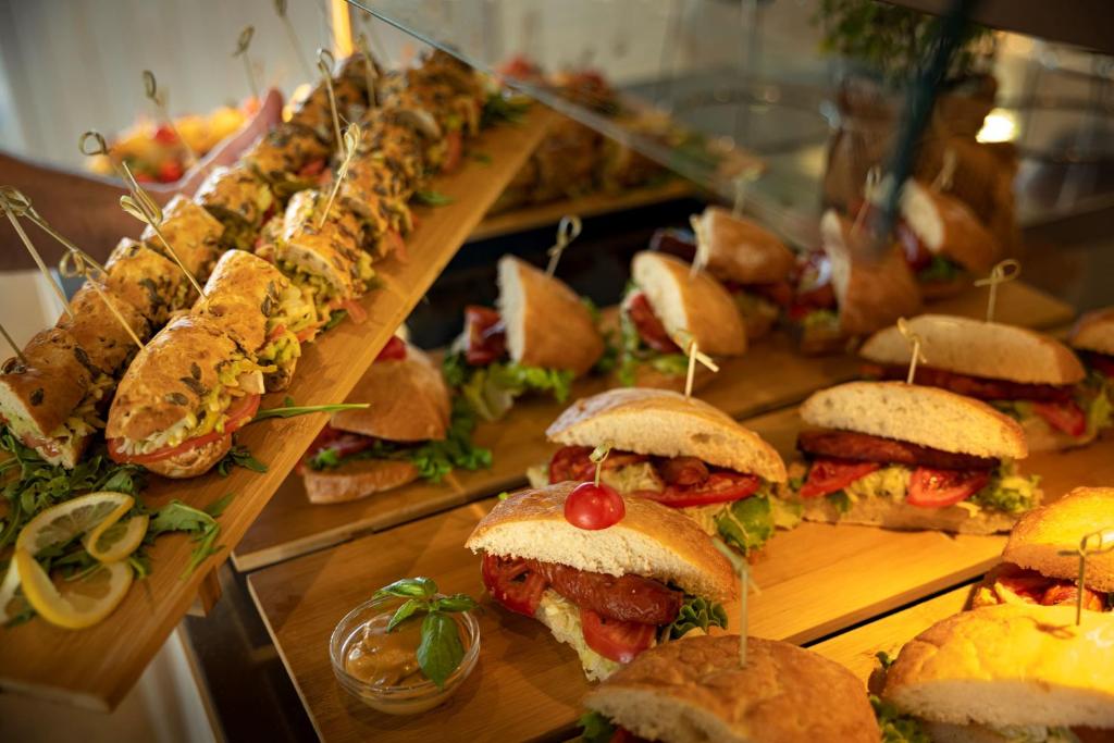 Svaigu un apetīti rosinošu sviestmaizes izvēle, kas pasniegta uz koka dēļa. Sviestmaizes ar dārzeņiem un gaļu, rotātas ar tomātiem un dekoratīvām iesmiņām.