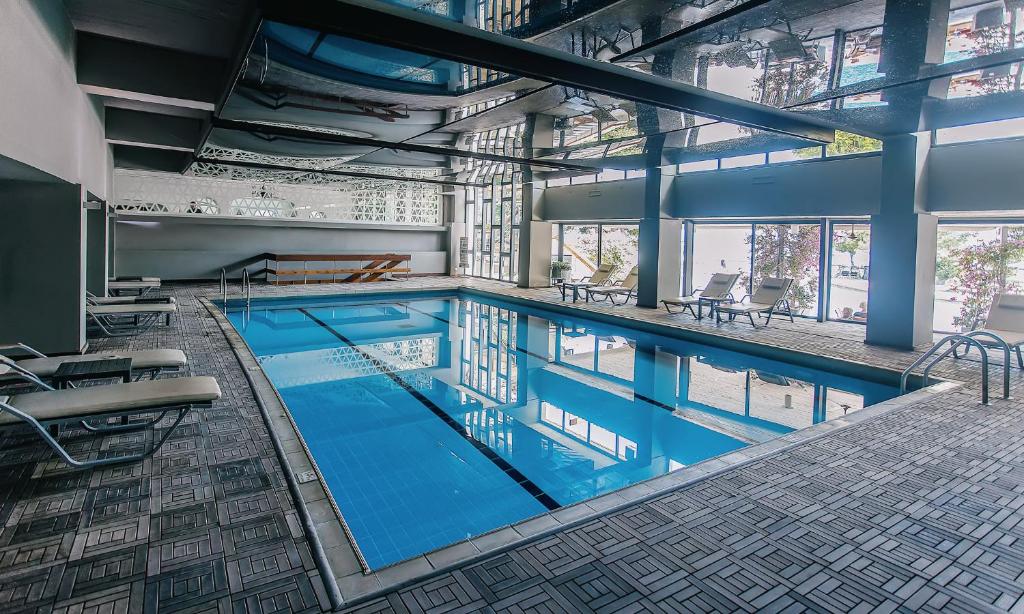 Iekštelpu baseins ar mūsdienīgu dizainu, apgaismots ar lieliem logiem, kas nodrošina dabisko gaismu. Ap baseinu novietoti atpūtas krēsli, radot relaksējošu atmosfēru.