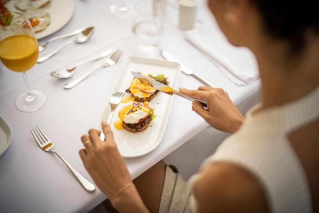 Gourmet brokastis ar olu un sagrieztiem augļiem, kas pasniegtas uz elegantas balto galda. Blakus glāze apelsīnu sulas.